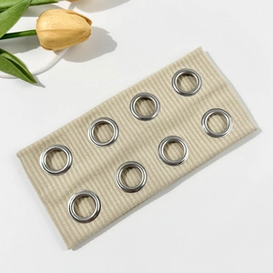 Detail of beige ribbed elastic headband with silver metal eyelets and soft knit texture