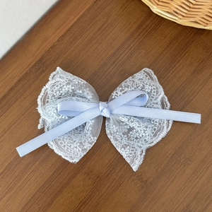 Elegant light blue lace bow hair clip with intricate embroidery on dark wooden background