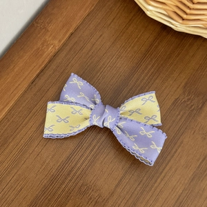Barrette à cheveux nœud bicolore violet et jaune avec bord froncé sur bois sombre