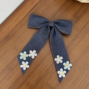 Détail de la pince à cheveux en denim avec broderies florales et coutures orange vif