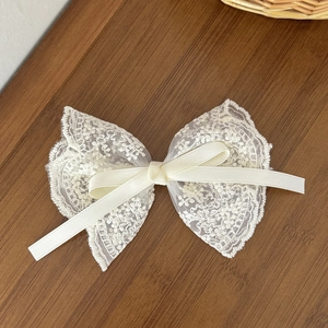 Detailed close-up of cream lace bow hair clip with satin ribbon on a rustic wooden table