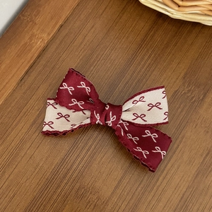 Détail d'une barrette à nœud bordeaux et crème avec texture jacquard sur bois