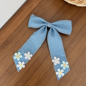 Détail d'un nœud de cheveux en denim bleu avec surpiqûres orange et broderies florales