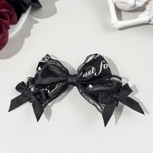 Detail of black lace and satin bow hair clip with decorative text and goth aesthetics