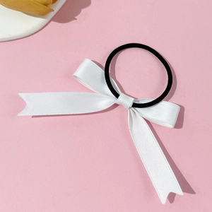 Detail of white satin bow hair tie with long ribbons on a pink textured background