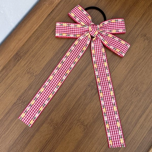 Détail d'un chouchou à nœud vichy rouge et blanc avec motif floral sur fond en bois