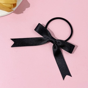 Detailed close-up of a black satin bow hair tie with polished ribbons on pink background