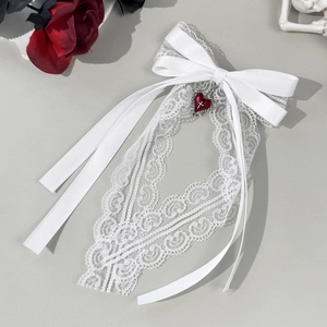 Détail du nœud en dentelle blanche avec un pendentif cœur rouge et rubans satinés