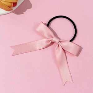 Pink ribbon bow hair tie with black elastic band on soft pink background with yellow flowers