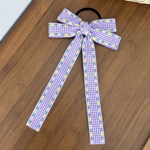Détail d'un chouchou noeud à carreaux violets avec bordure fleurie sur fond en bois