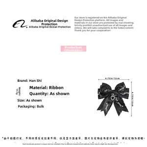 Detail of a black ribbon bow hair clip featuring heart pendant and letter print