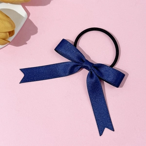 Close-up of a navy blue bow hair tie with long ribbons on a pink background