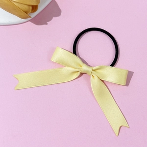 Sweet light yellow satin bow hair tie with black elastic band on soft pink background