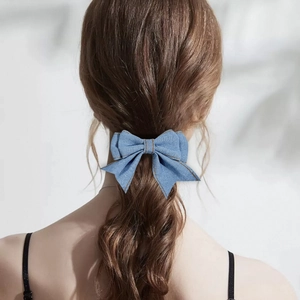 Detail view of denim bow hair clip with orange stitching on model's hair