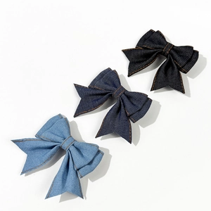 Three denim bow hair clips in light, medium, and dark blue with orange contrast stitching
