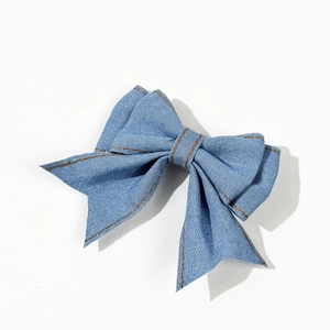 Denim bow hair clip with orange contrast stitching and hanging ribbons on white backdrop