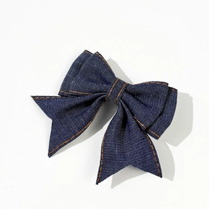Detail of dark blue denim bow hair clip with contrasting orange stitching on white background