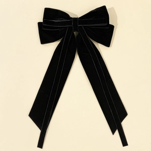Detailed view of the layered black velvet bow with long flowing ribbons on a beige background
