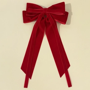 Detail of a large red velvet hair bow clip with long ribbons on a cream background