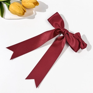 Detail of burgundy satin ribbon hair bow with long streamers on a minimalist background