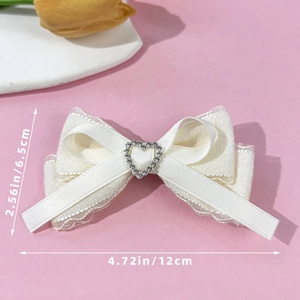 Cream ballet style bow hair clip with heart rhinestone center on pink background