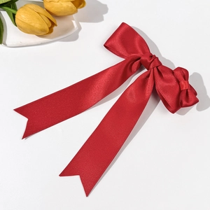 Detail of red satin bow hair clip with long ribbons on white surface with tulips