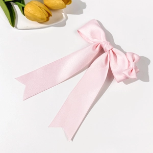 Elegant pink satin ribbon bow hair clip with long streamers on a white background