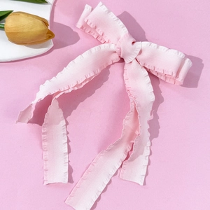 Close-up of pink bow hair clip featuring pleated edges and textured fabric ribbon detail