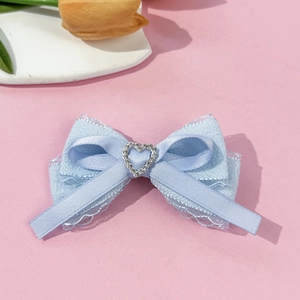 Detail of light blue satin bow hair clip with heart-shaped silver rhinestones on pink background