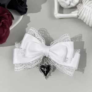 Close-up of a white lace bow hair clip featuring a black heart and silver cross pendant
