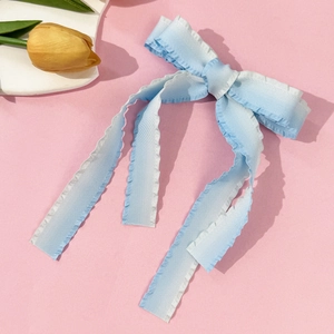 Blue and white gradient bow hair clip with long ribbons on a soft pink background