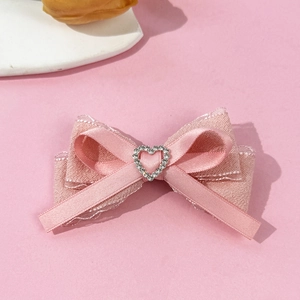 Close-up of pink ribbon hair clip featuring a lace edge bow and heart-shaped rhinestone buckle
