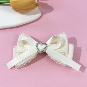 Detail of cream white bow hair clip with layered satin lace and rhinestone heart center