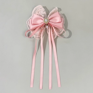 Detail of pink layered lace bow hair clip featuring a central pearl and long satin ribbons