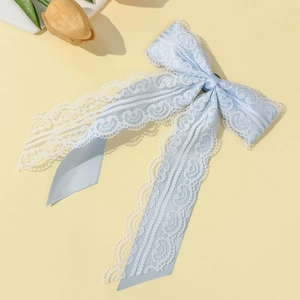 Detail of light blue lace bow brooch with long ribbons on a soft yellow background