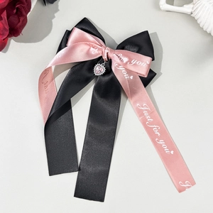 Dettaglio del fermaglio con fiocco in raso rosa e nero e ciondolo a cuore in strass