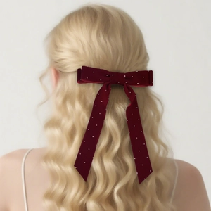 Elegant burgundy velvet bow hair clip with white polka dots on long wavy blonde hair