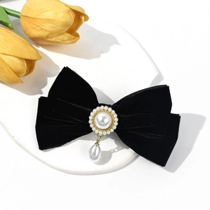 Detail of velvet bow hair clip with pearl pendant and golden accents on ceramic tray
