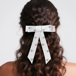 Detail of white satin bow hair clip with silver heart studs on wavy long hair