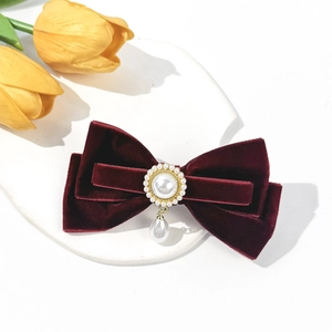 Detail of burgundy velvet bow hair clip with pearl pendant on a white stone base