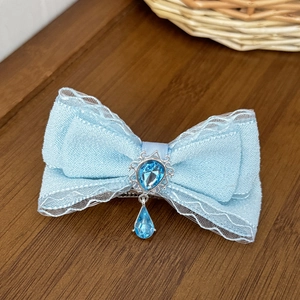 Detail of light blue lace bow hair clip with teardrop gemstone pendant on wood texture