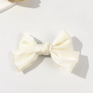 Detailed view of glossy cream white satin bow hair clip with smooth fabric texture