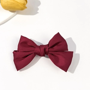 Detail view of a wine red satin bow hair clip on white background with yellow tulips