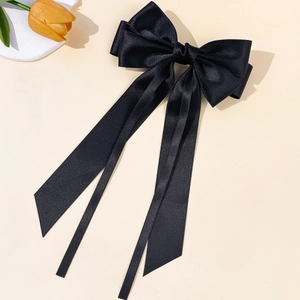 Macro view of black satin bow hair clip with long ribbons on a floral background