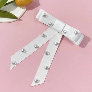 Detailed macro view of white satin bow with silver heart beads on a soft pink background