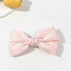 Detailed close-up of a pink satin double-layered bow hair clip on a white surface
