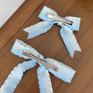 Blue and white gradient bow hair clips with wavy edges on a wooden surface