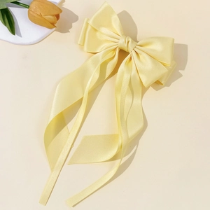 Detail of light yellow satin bow hair clip with long ribbons and elegant silk texture