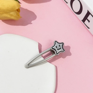 Detail shot of a silver star hair clip with a smiley face design on a pink background