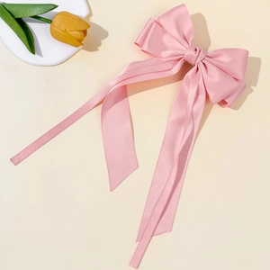 Close-up of a large pink satin bow hair clip with long streamers in a soft lighting